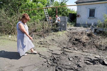 Archivbild: Eine Frau zeigt einen Bombentrichter nach einem ukrainischen Angriff auf die Stadt Jassinowataja, 18. Juni 2023. Bild: SERGEI AWERIN / Sputnik